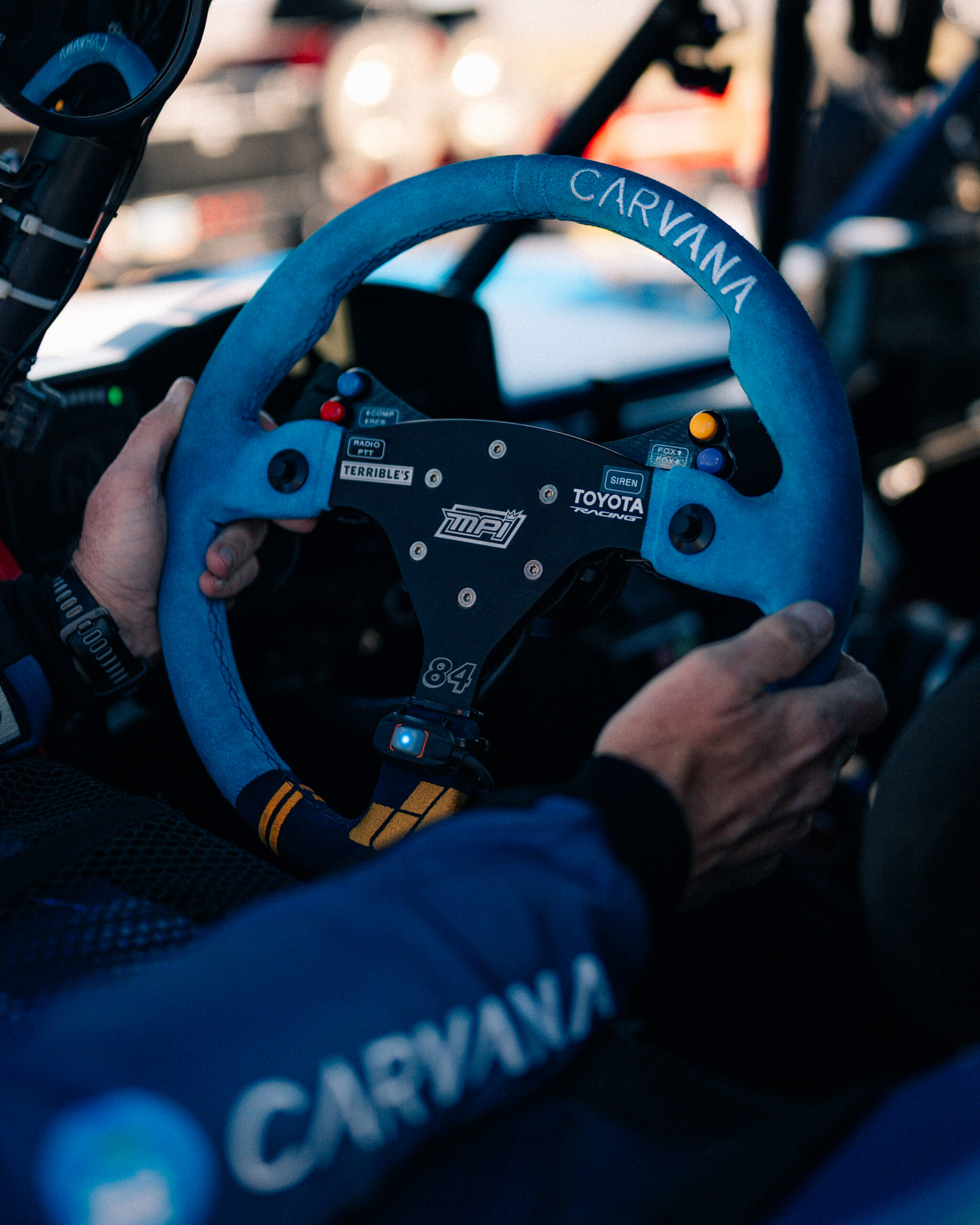 Close-up of hands on a Carvana-branded steering wheel inside the No. 84 Terrible Herbst Motorsports off-road truck during the Mint 400.