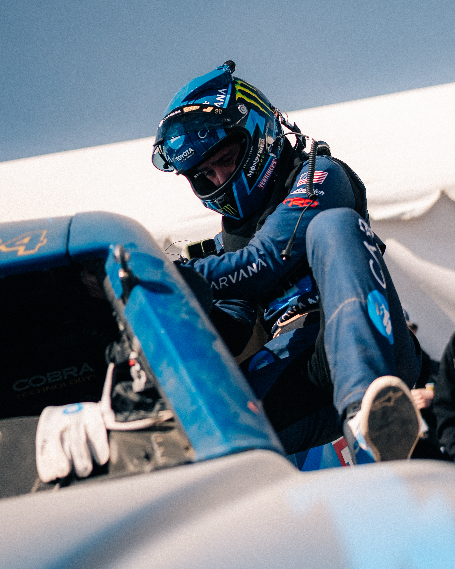 Driver in a Carvana-branded helmet and race suit climbing into the Carvana-sponsored No. 84 Terrible Herbst Motorsports off-road truck before the Mint 400 in Nevada.