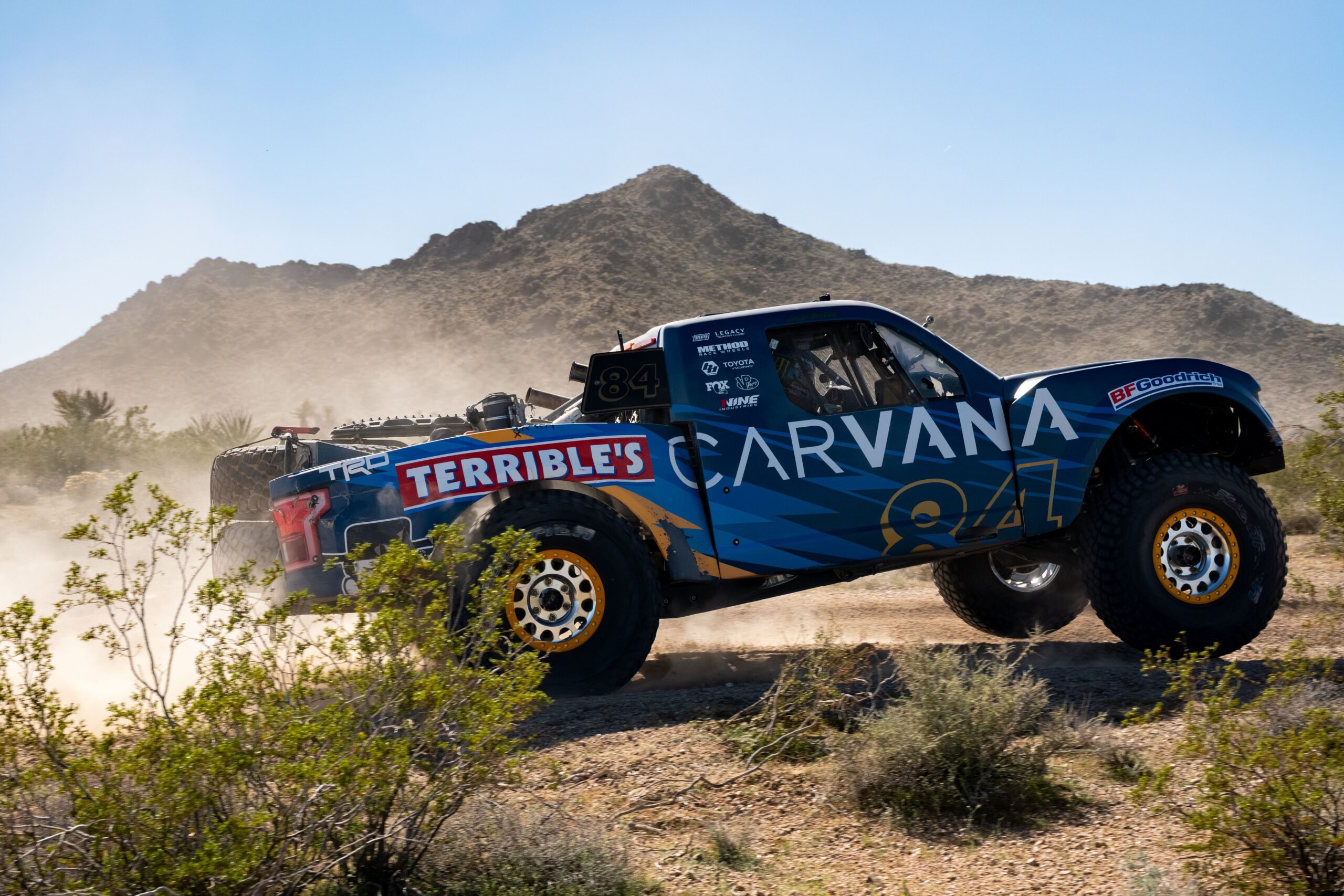 Carvana-sponsored Terrible Herbst Motorsports off-road truck driving past desert plants and mountains during the BFGoodrich Mint 400 in Nevada.