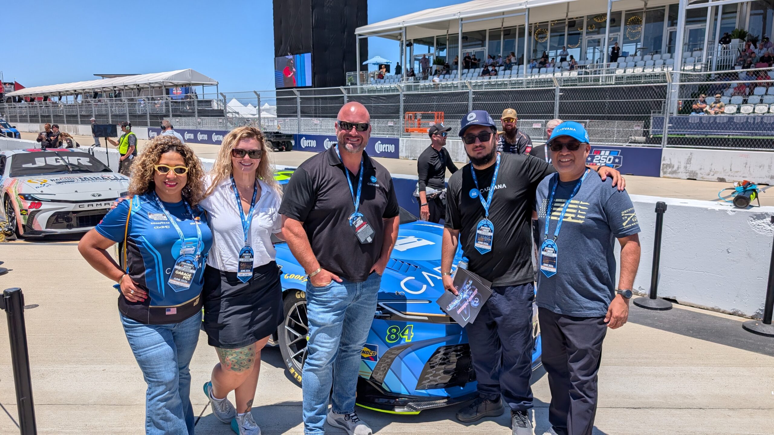 Carvana CarVets members pose in front of the No. 84 Carvana Toyota Camry XSE in the garage area at Naval Base Coronado ahead of the Anduril 250.