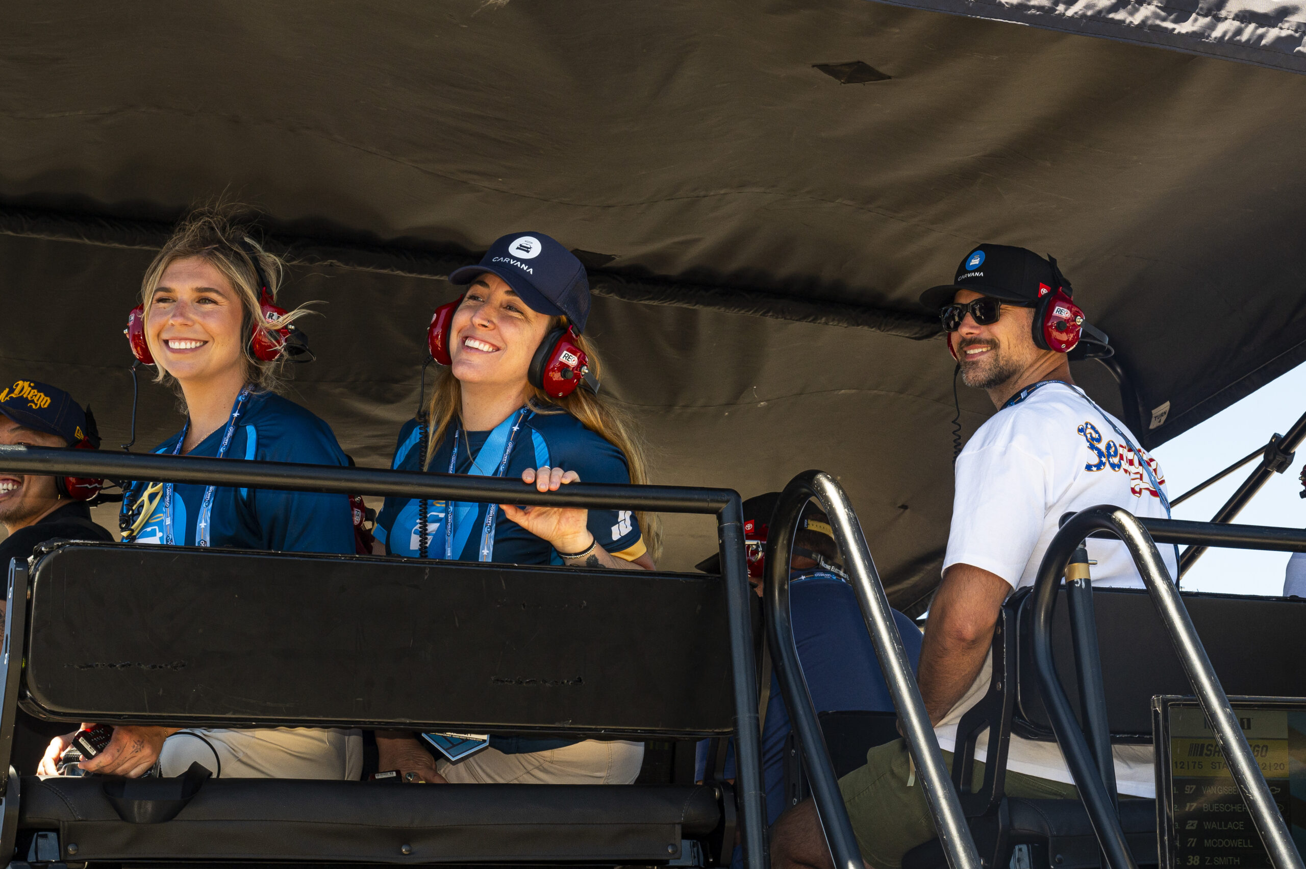 Carvana employees wearing race headsets and Carvana caps watch the Anduril 250 from the Legacy Motor Club hospitality area at Naval Base Coronado.