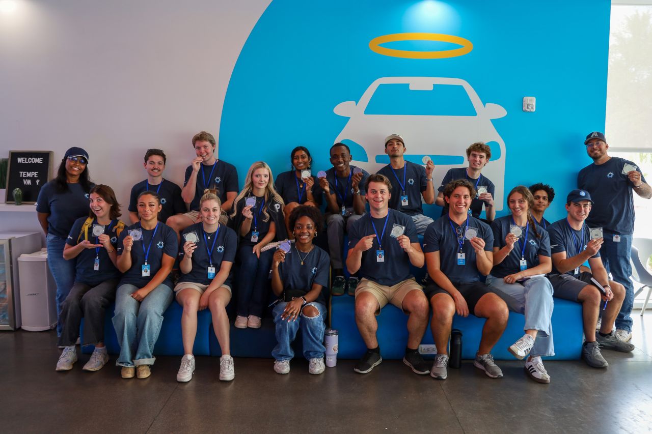 Carvana Customer Care interns gather at the Tempe Car Vending Machine, holding commemorative coins after learning how this signature location fits into the customer journey.