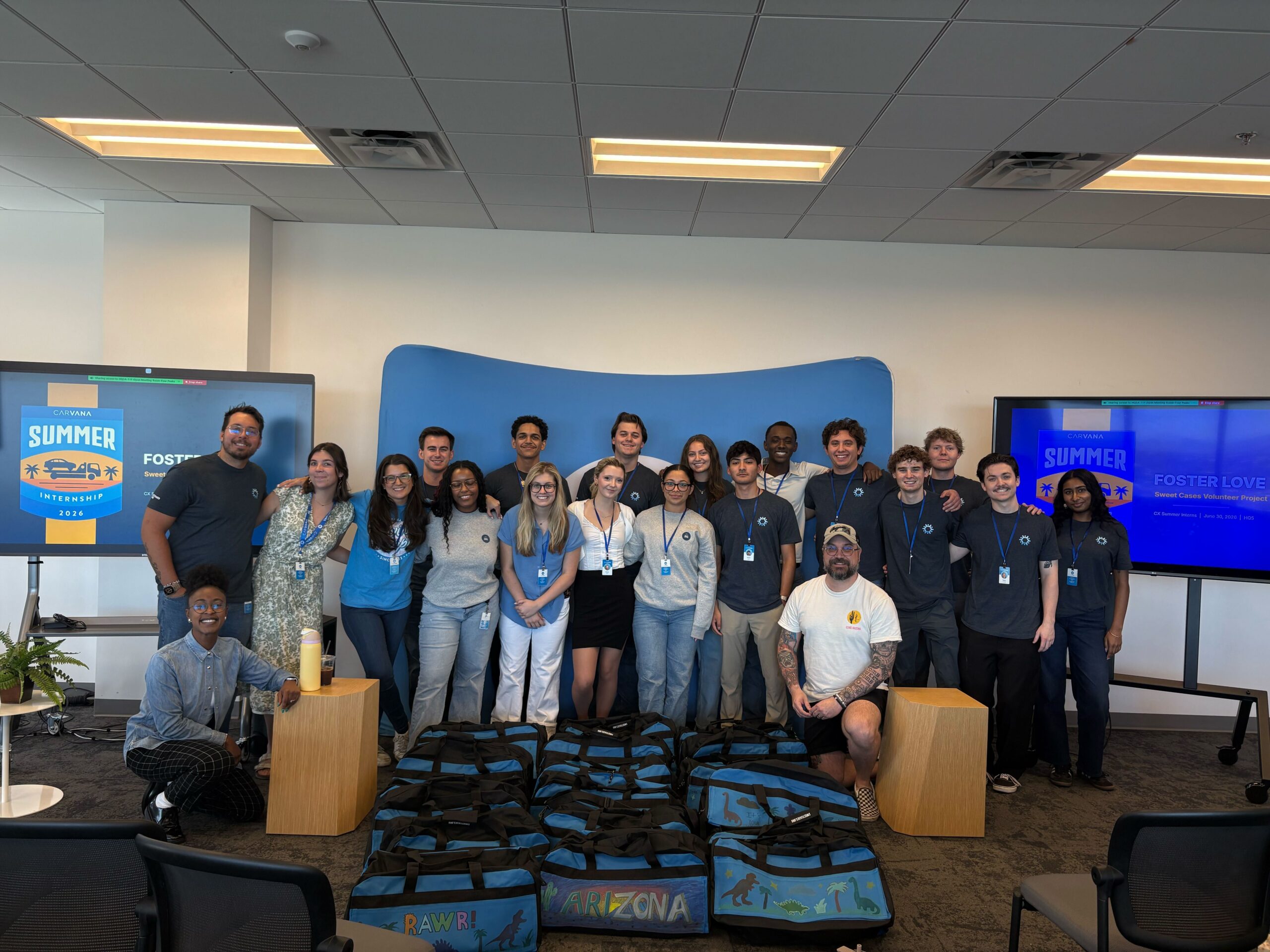 Carvana Customer Care interns and team members celebrate completing a summer volunteer project, posing behind decorated duffel bags created for children in foster care.